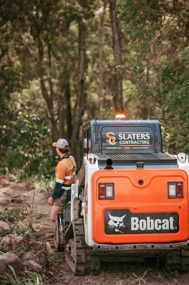 Slaters Bobcat track loader on a bush block, with a worker beside it