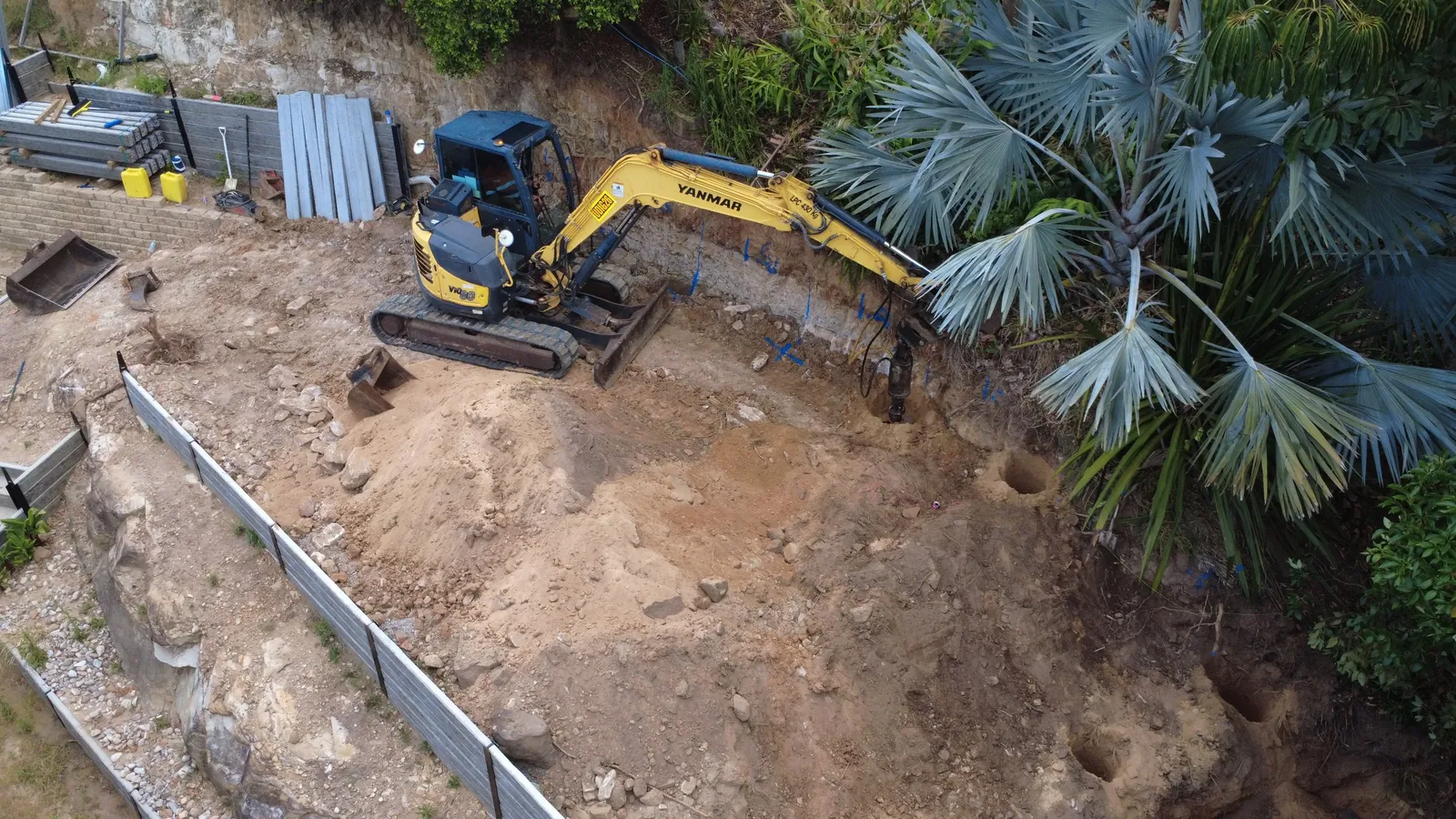 Drone view of an excavator digging behind a new sleeper retaining wall