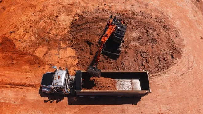 Drone view looking straight down on an excavator loading a tipper on a red-dirt site
