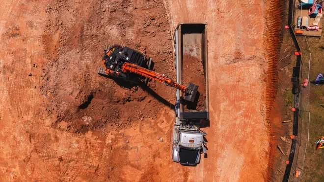 Drone view of an excavator filling a tipper beside the site fence