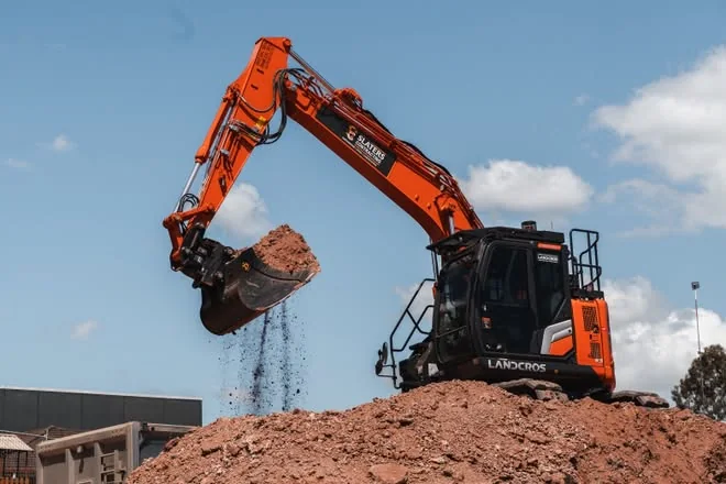 Slaters excavator lifting a full bucket of dirt off a spoil pile