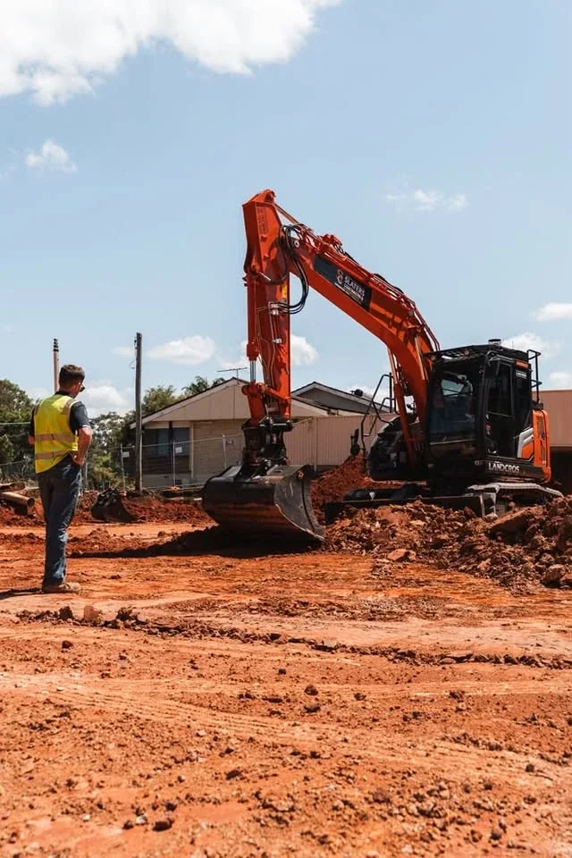 Worker in hi-vis watching a Slaters excavator on a site cut