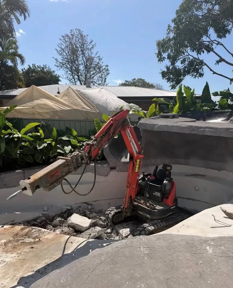 Mini excavator with a rock breaker taking out an old pool